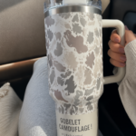 Une tasse Stanley au motif camouflage exposée sur une table en bois.